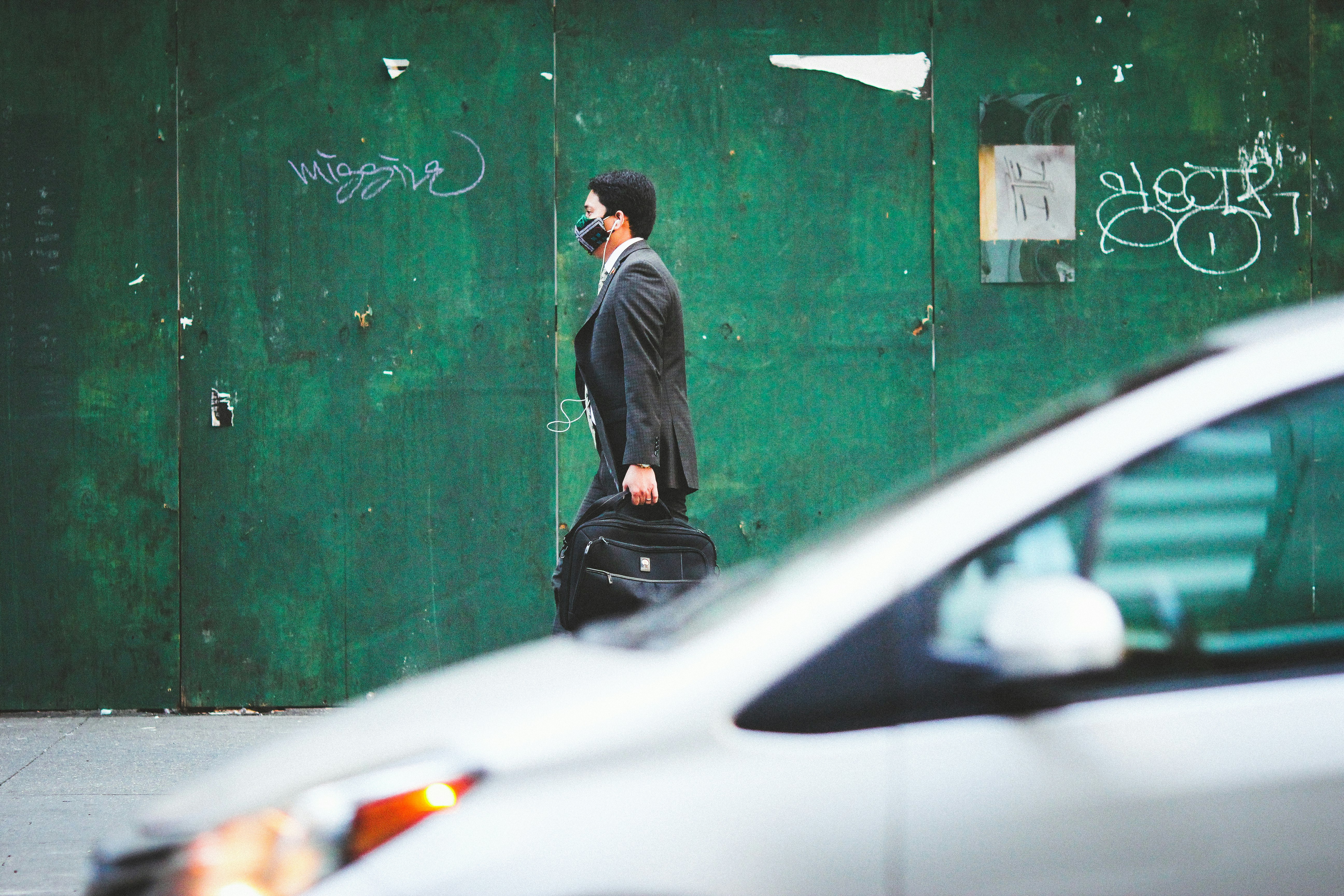 man in black suit standing beside green wall